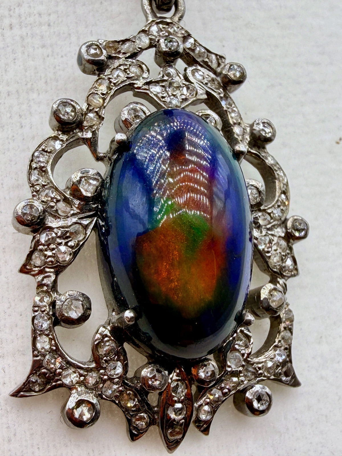 Close-up of 6.75 carat Australian black opal pendant showing blue green red and orange play-of-color with diamond accents