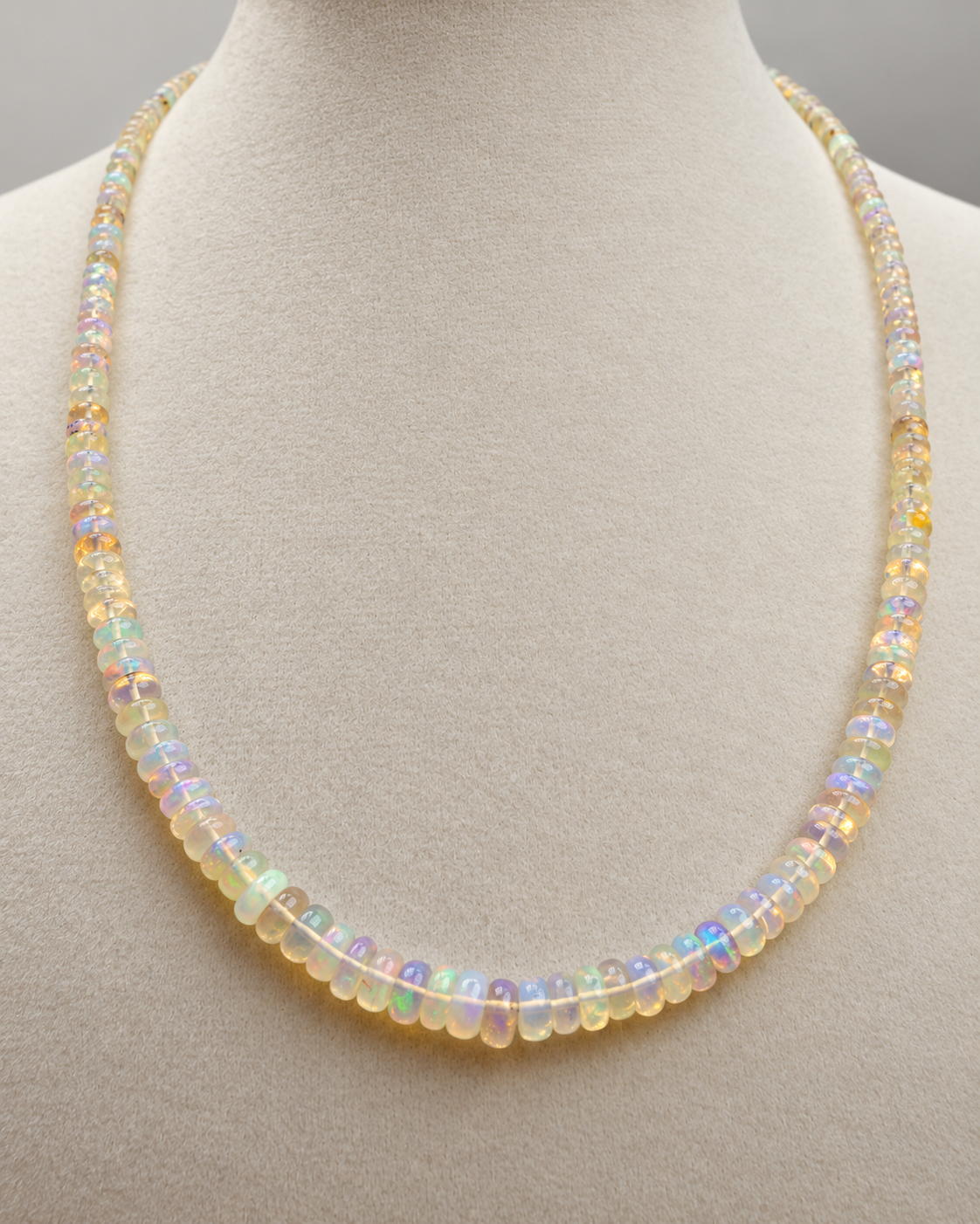 18 inch Ethiopian opal bead necklace with iridescent rondelle opals displayed on a cream jewelry bust