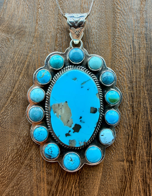Handcrafted stainless steel Southwestern pendant featuring a large natural turquoise center stone surrounded by a turquoise cluster with decorative engraved bail